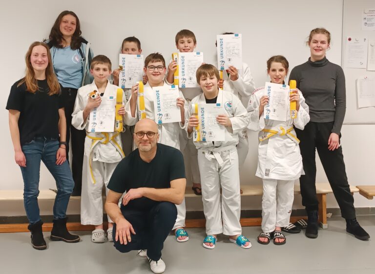 Gruppenbild. Kinder, Trainer und Prüflinge lächeln in die Kamera. Die Kinder halten ihre Urkunden in den Händen